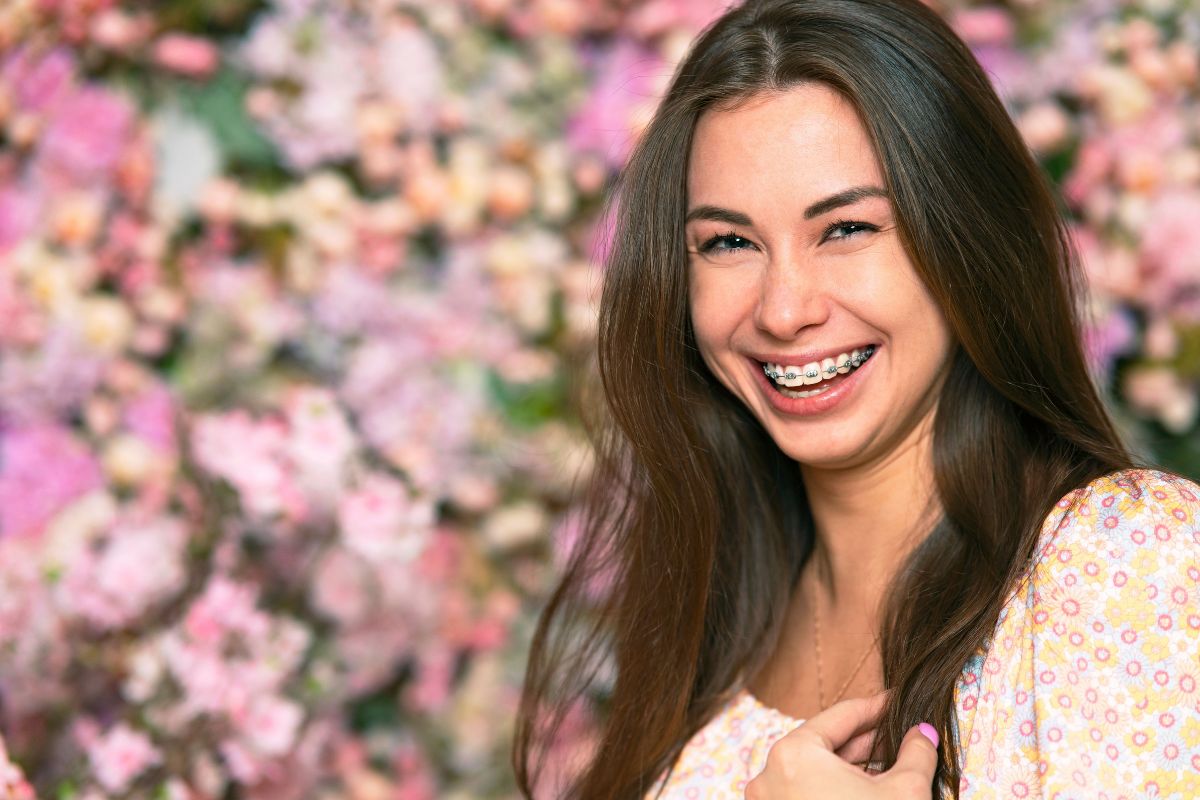 Spring Braces Colors Woman smiling at camera with pink floral background in dental office setting.