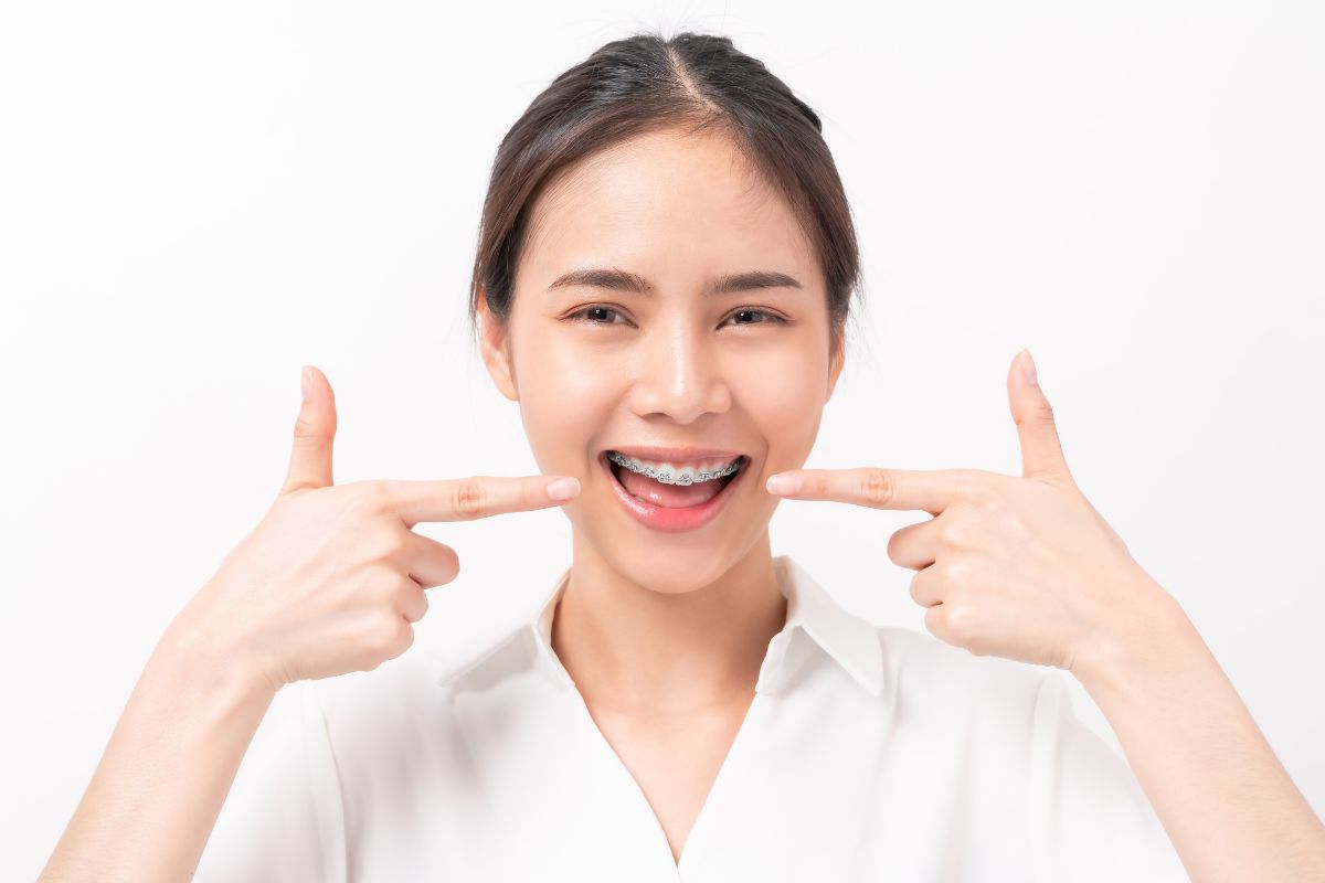 Woman pointing at her smile wearing white shirt against white background